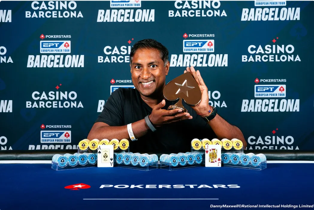 Vinny Lingham holding the EPT Barcelona trophy behind stacks of chips